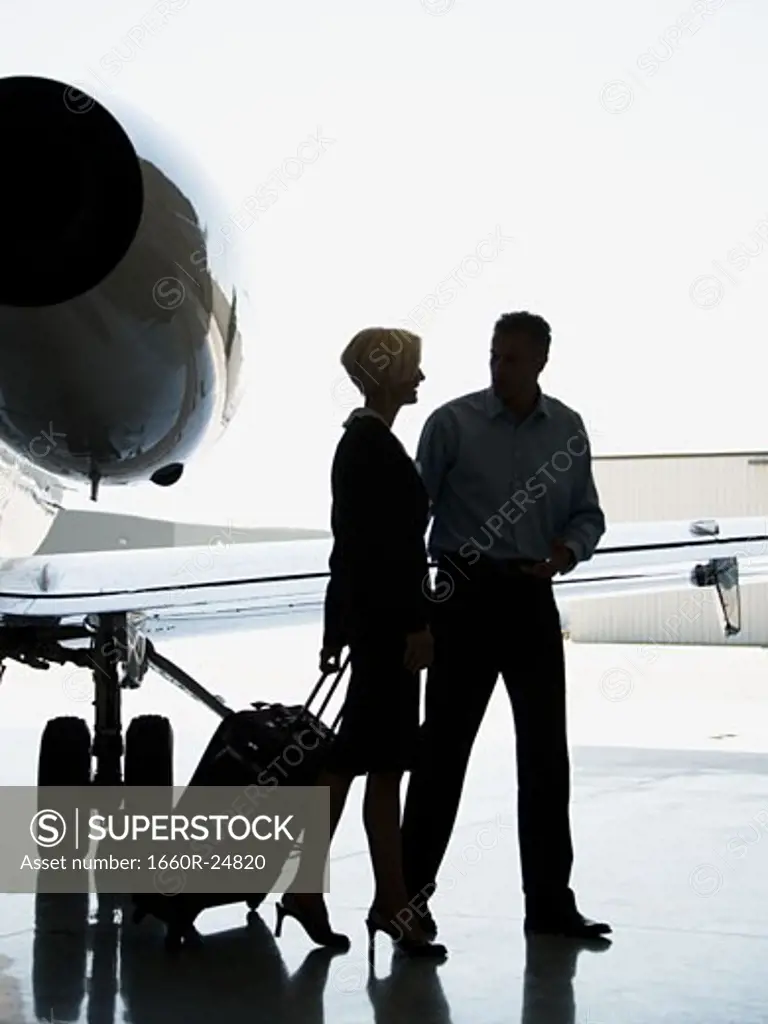 Profile of a businesswoman and a businessman walking with suitcases by an airplane