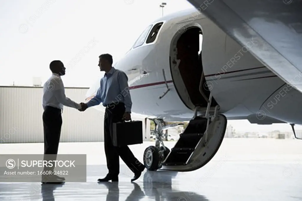 Profile of two businessmen shaking hands by an airplane