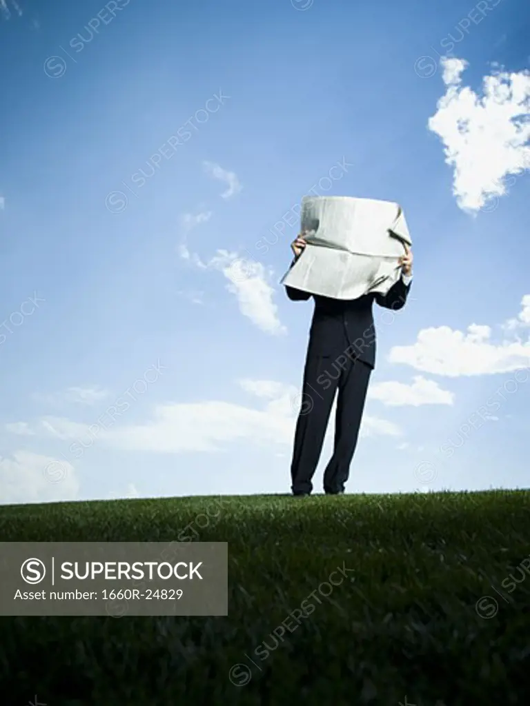 Businessman standing on the grass and reading a newspaper