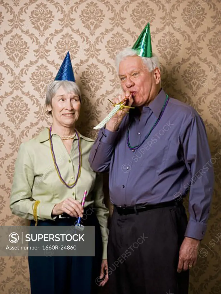 A senior man standing with a senior woman and blowing a party favor