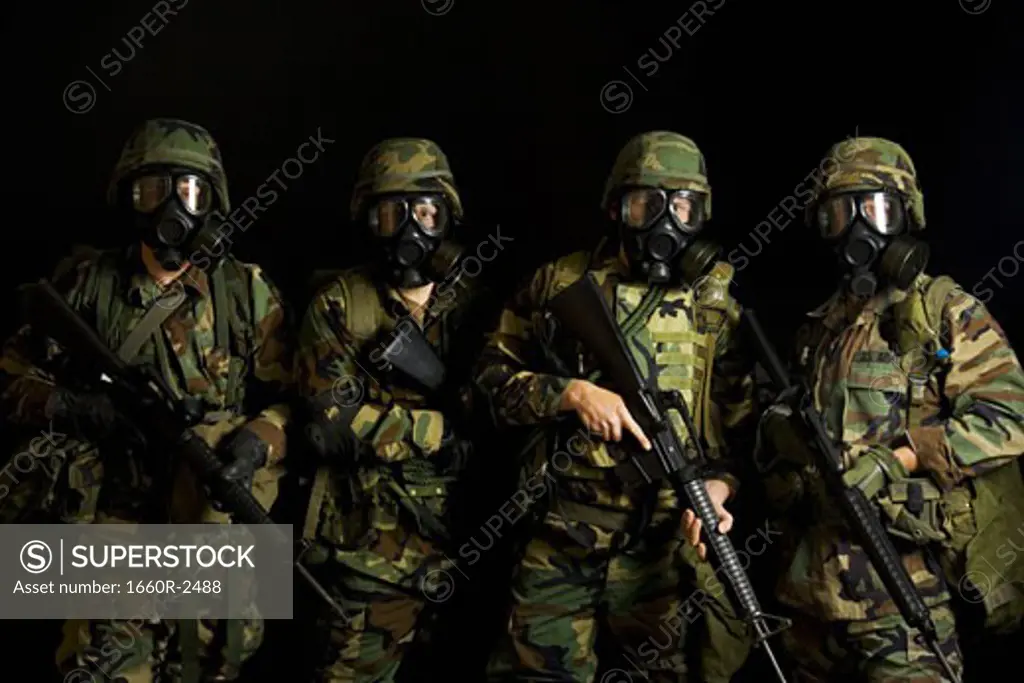 Four soldiers wearing gas masks and holding rifles