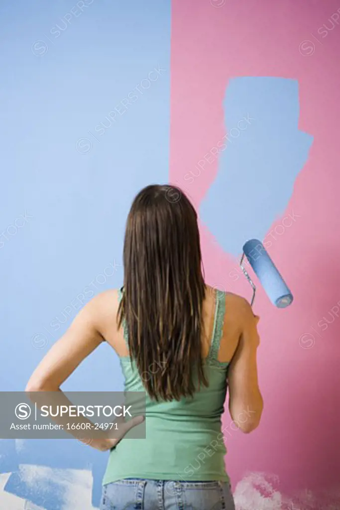 Rear view of woman painting wall with a paint roller