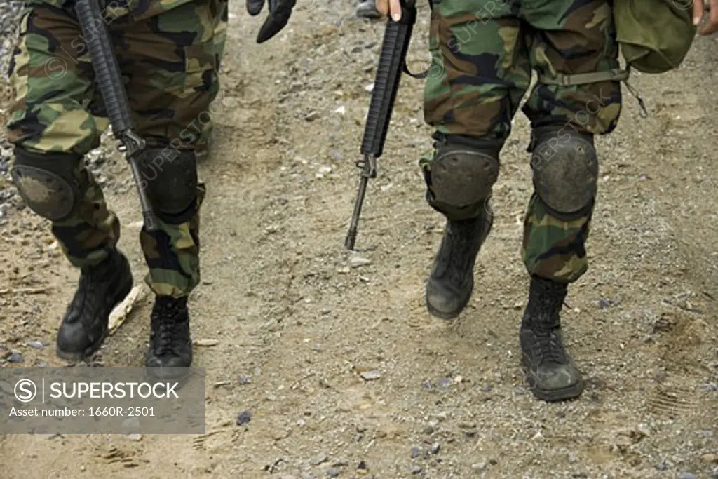 Low section view of two soldiers walking with their rifles