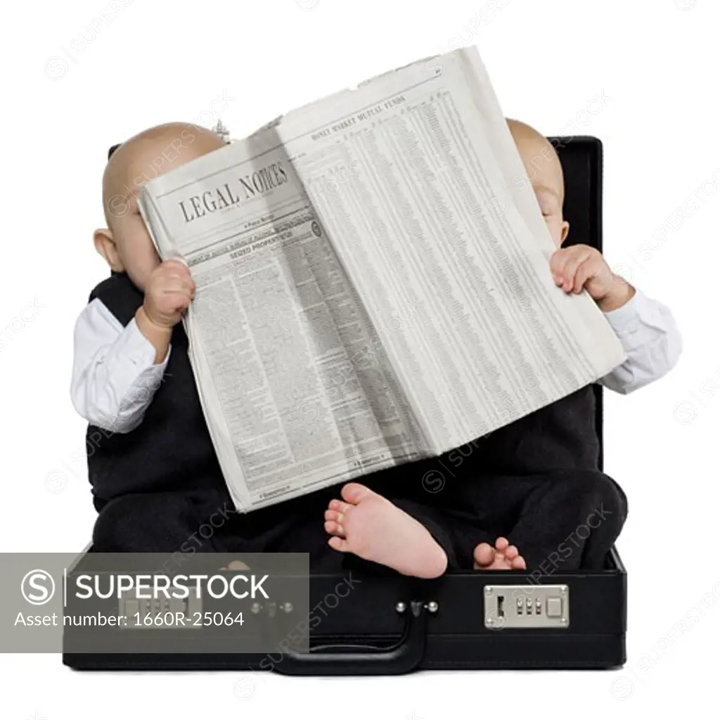 Twin boys sitting in a briefcase with newspaper