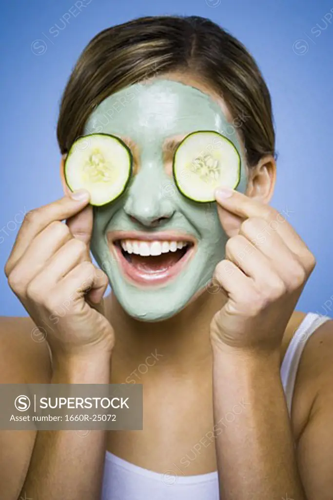 Woman with mud mask and cucumber slices smiling