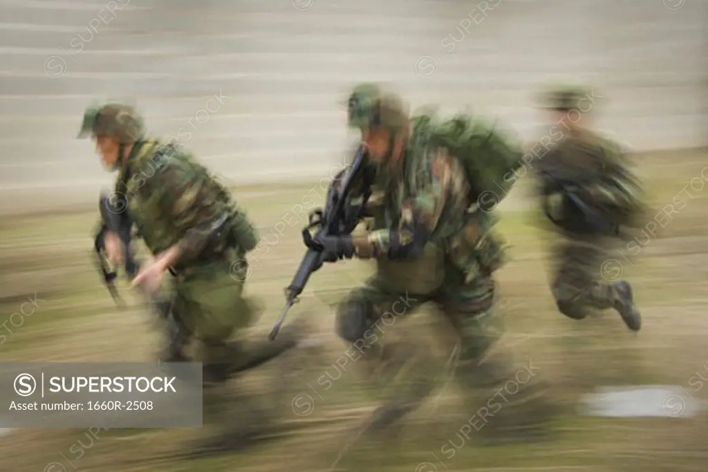 Three soldiers running on the field with their rifles