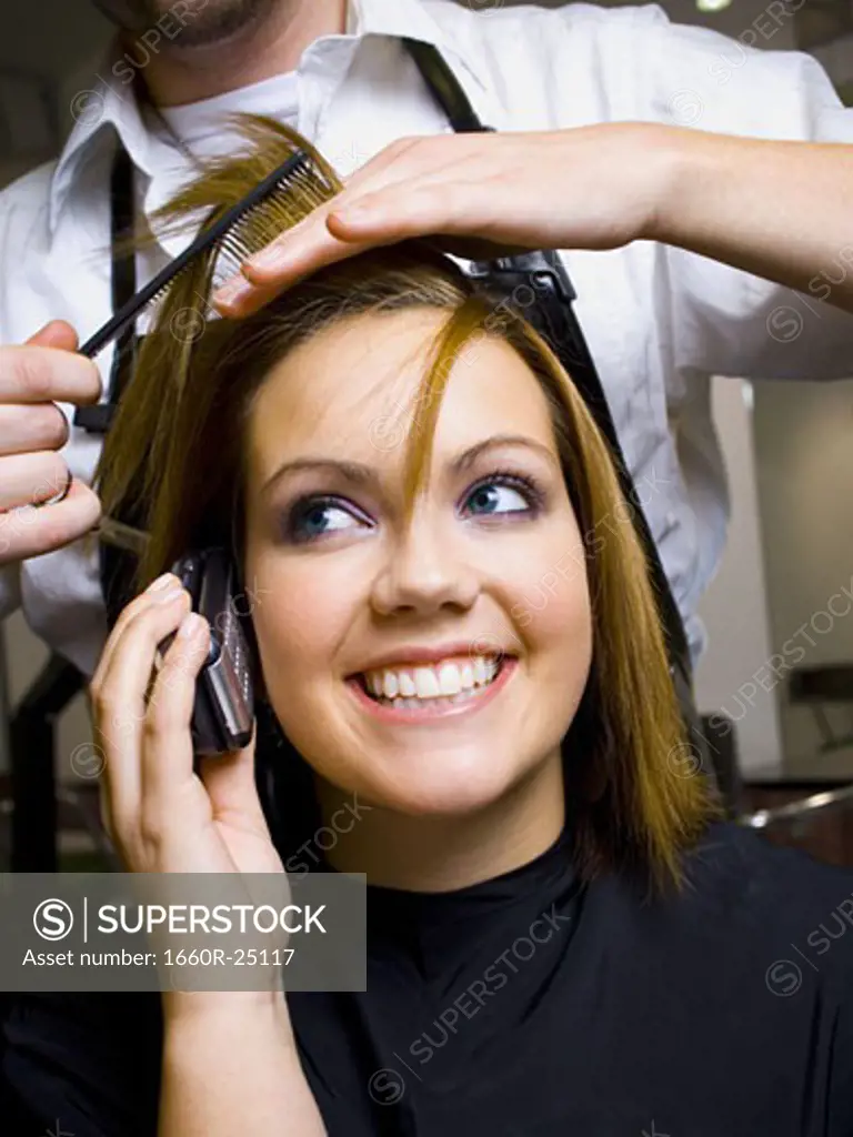 Woman on cell phone smiling while having hair cut