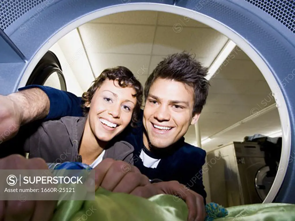 Young couple taking clothes out of dryer at Laundromat smiling
