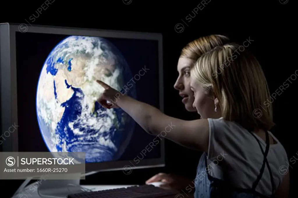 Two girls looking at earth on computer monitor