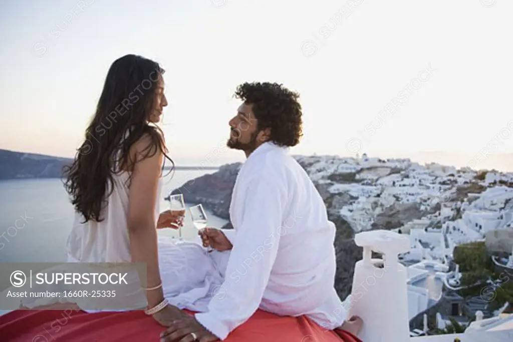Couple sitting outdoors with champagne flutes and scenic background smiling
