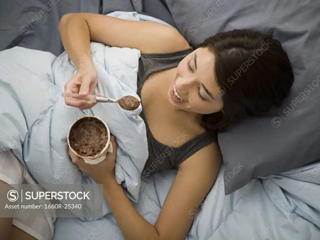 Woman lying down in bed spilling chocolate ice cream on blanket
