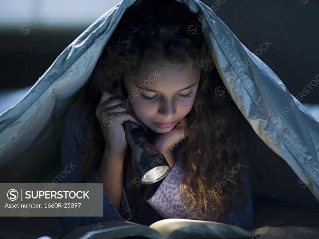 Girl laying in bed under blanket with flashlight reading
