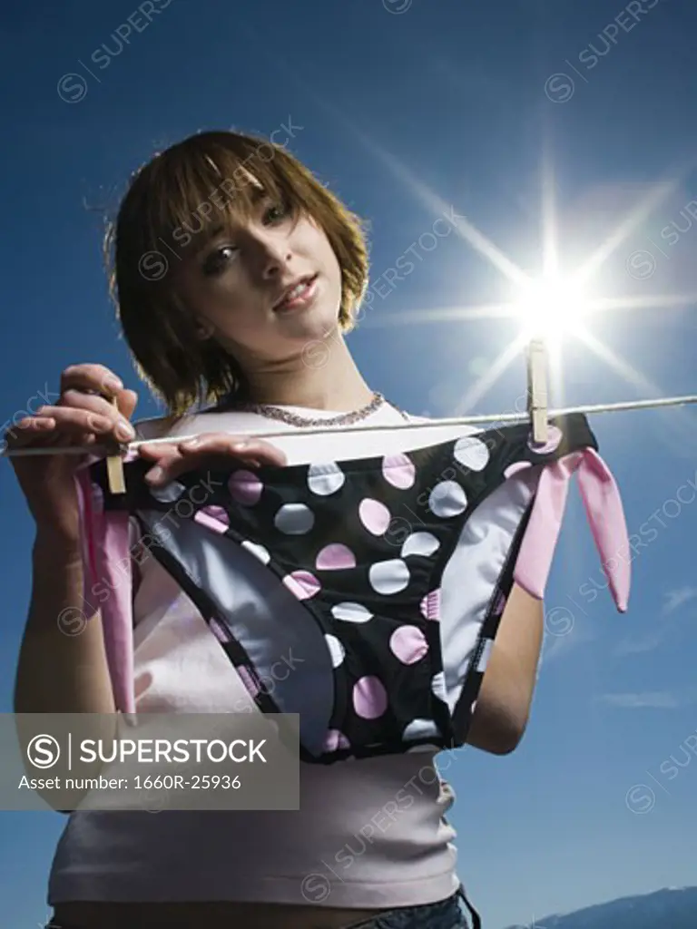 Low angle view of a teenage girl drying a bikini bottom on a clothesline