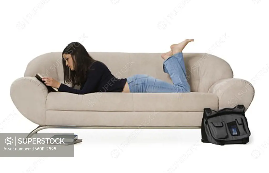 Side profile of a young woman lying on a couch and reading a book