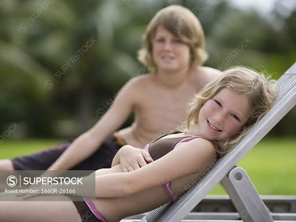 Portrait of a girl reclining on a lounge chair with her brother behind her