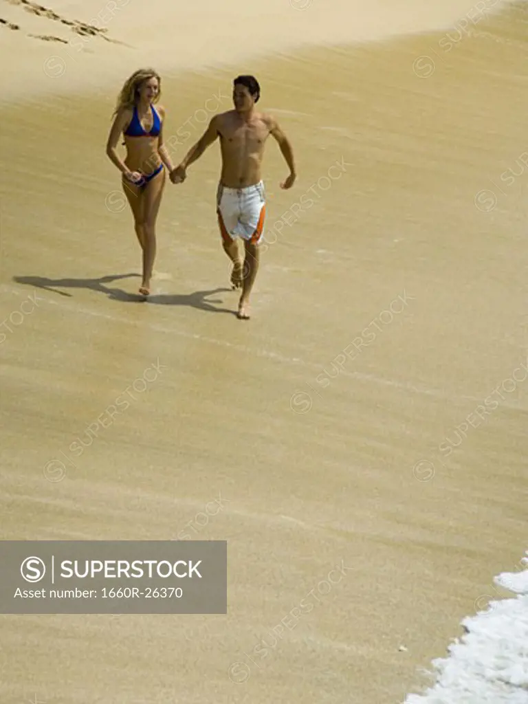 High angle view of a young couple holding hands and running on the beach