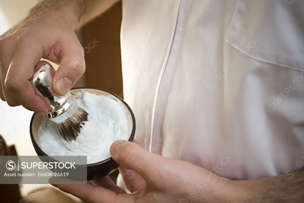 Mid section view of a man's hand mixing shaving cream with a brush in a bowl