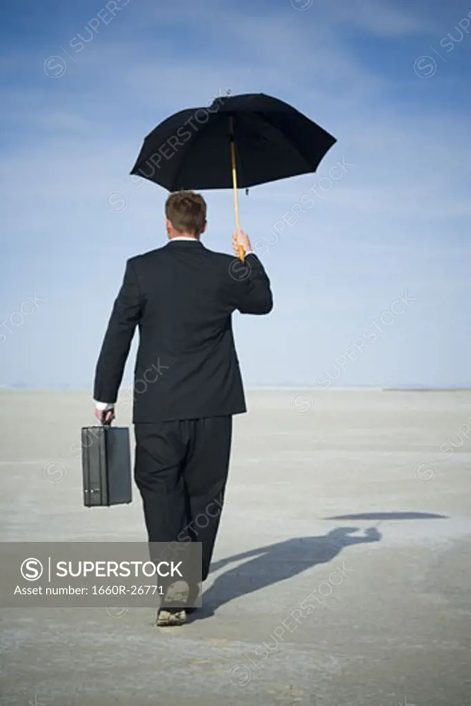 Rear view of a businessman walking and holding an umbrella