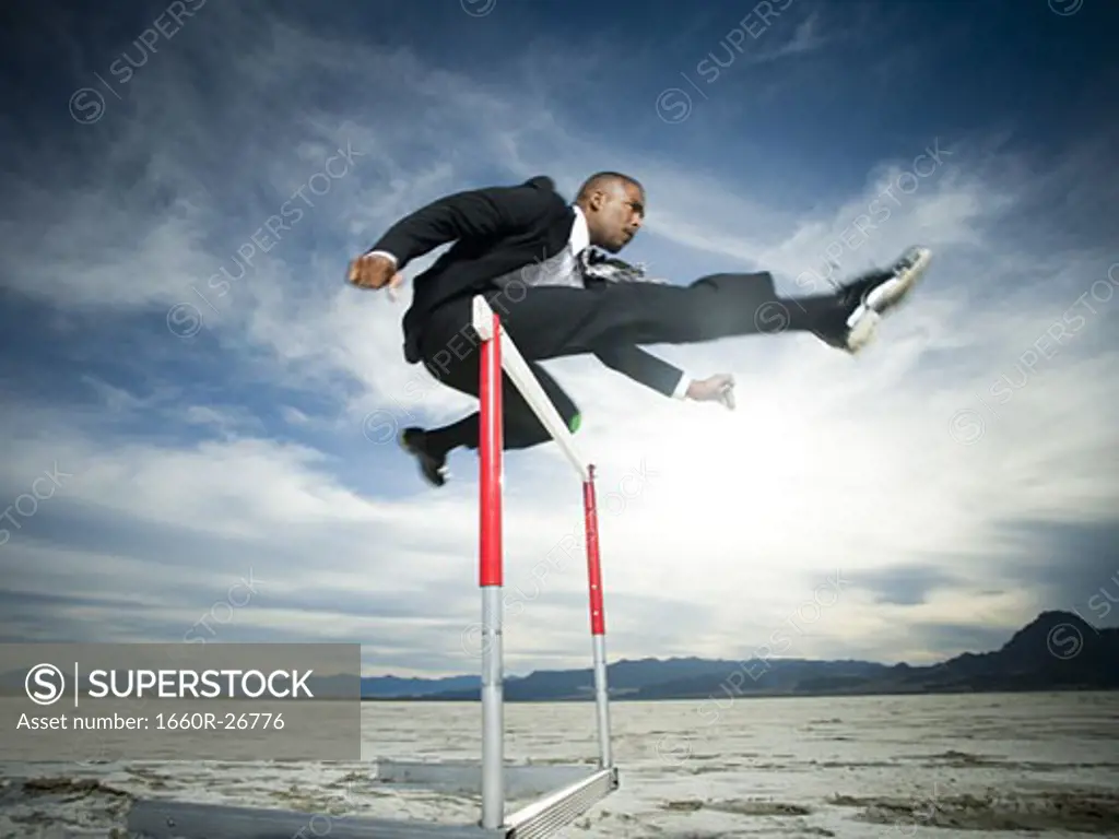 Low angle view of a businessman jumping over a hurdle in a race