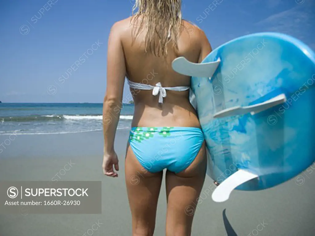 Rear view of a young woman holding a surf board
