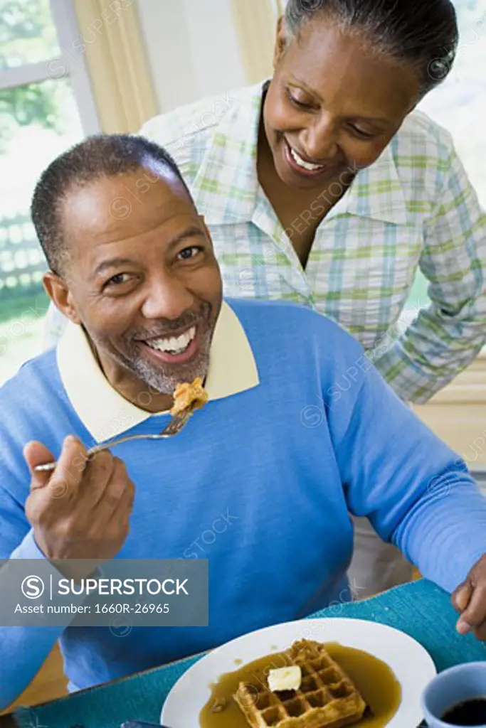 Close-up of a senior man having breakfast with a senior woman behind him