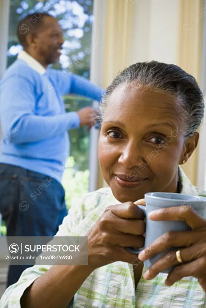 Close-up of a senior woman holding a cup of coffee with a senior man standing behind her