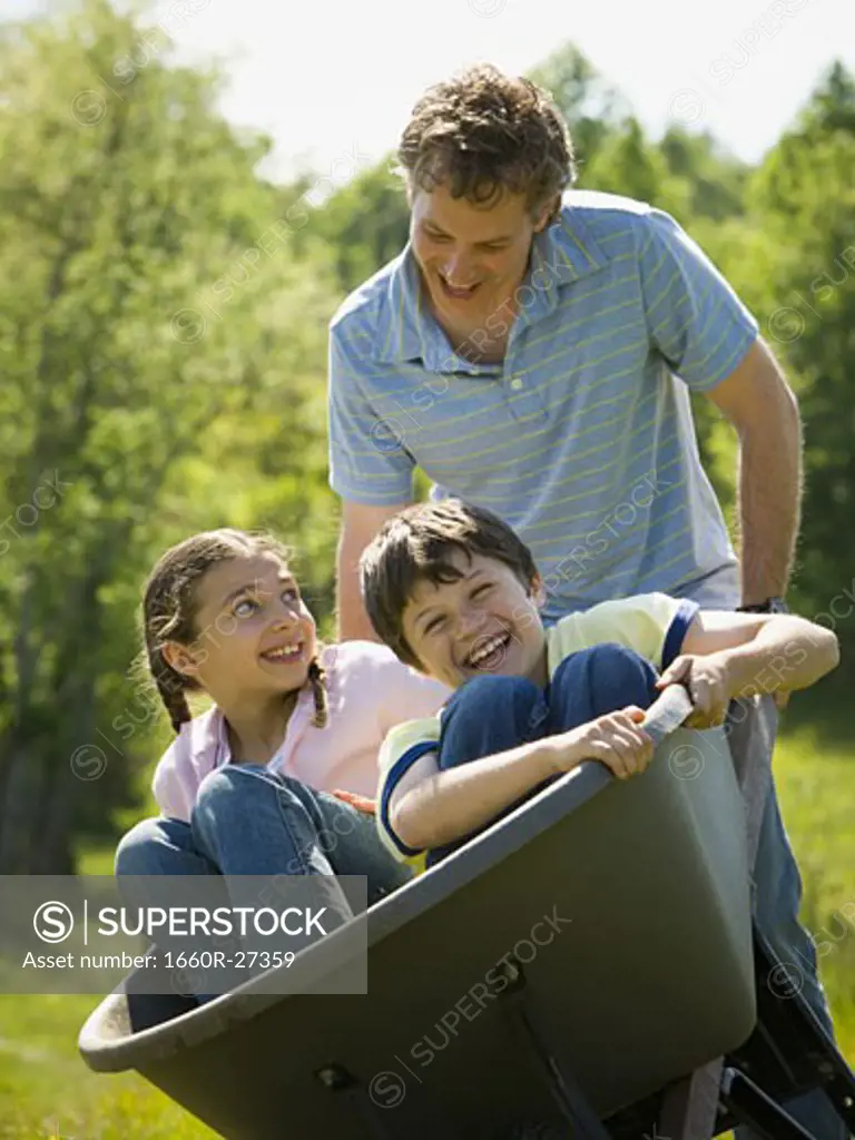 man pushing his son and daughter in a wheelbarrow