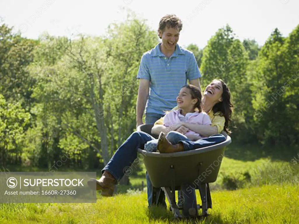 man pushing his daughter and his wife in a wheelbarrow