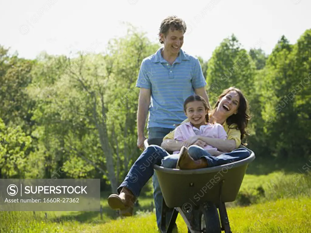 man pushing his daughter and his wife in a wheelbarrow