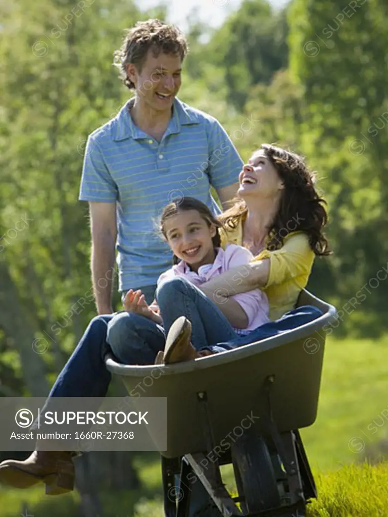 woman and her daughter sitting in a wheel barrow with a man standing beside them