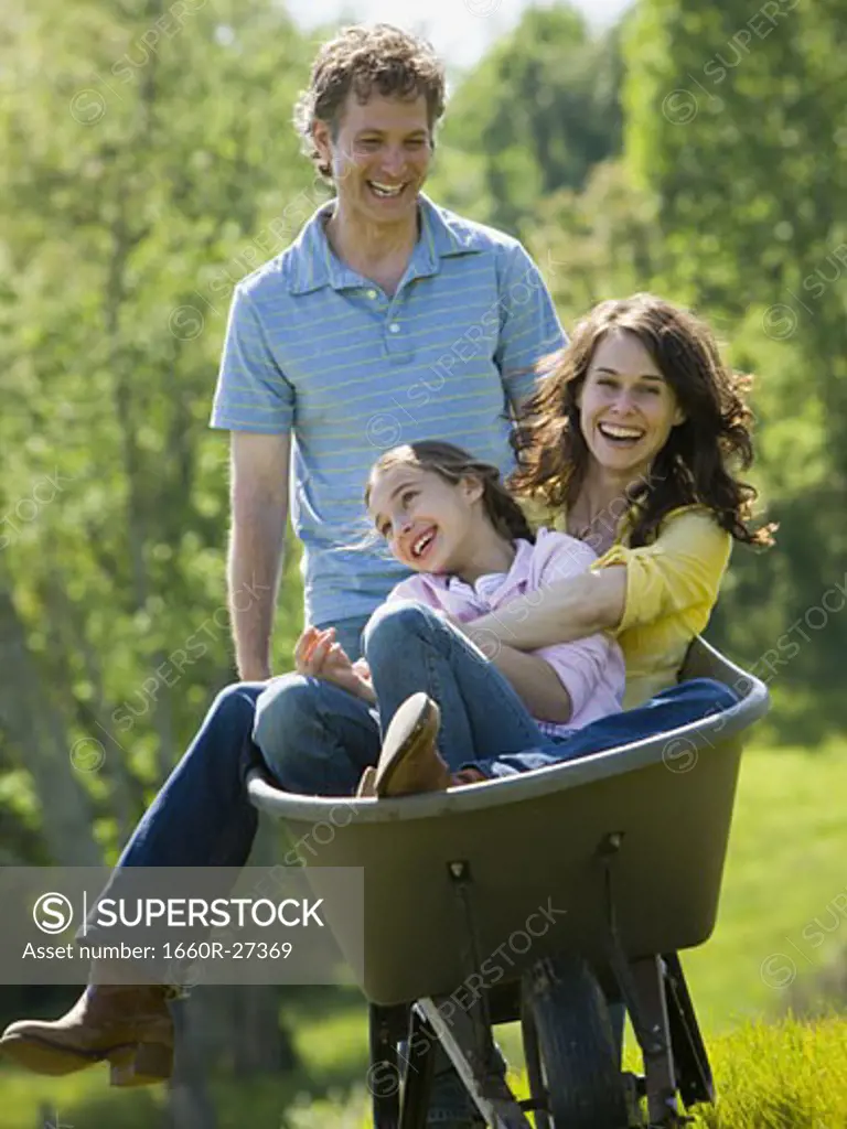 woman and her daughter sitting in a wheel barrow with a man standing beside them