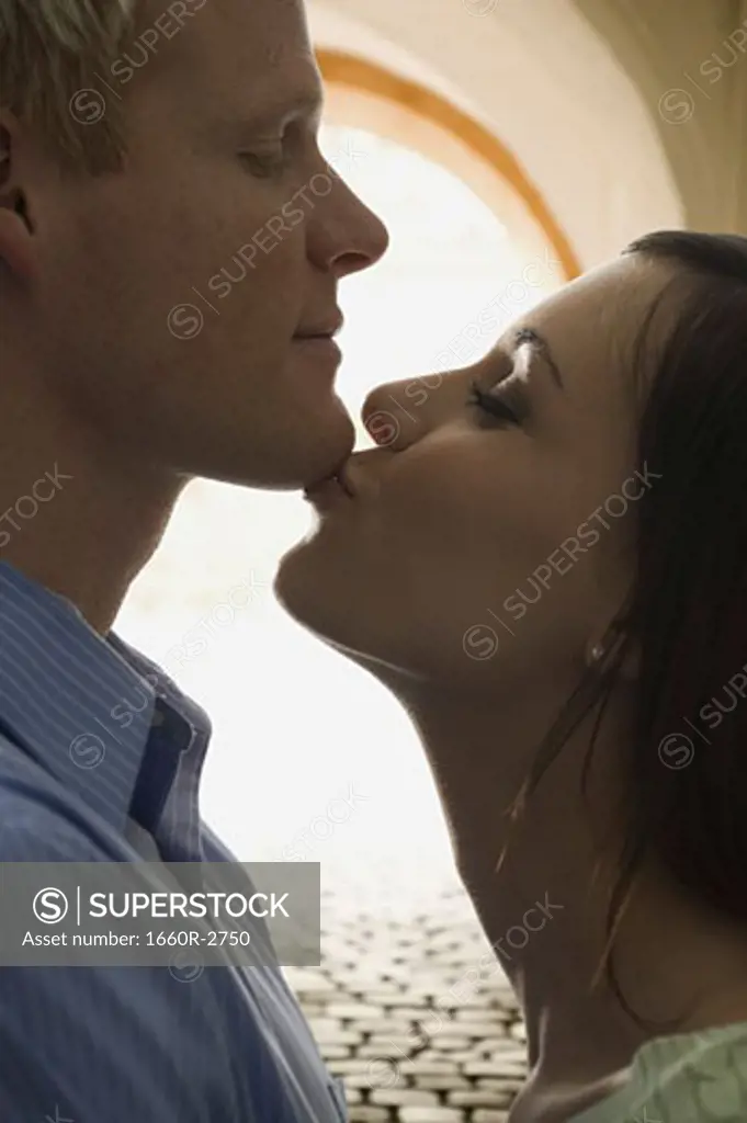 Side profile of a young woman kissing a young man on his chin