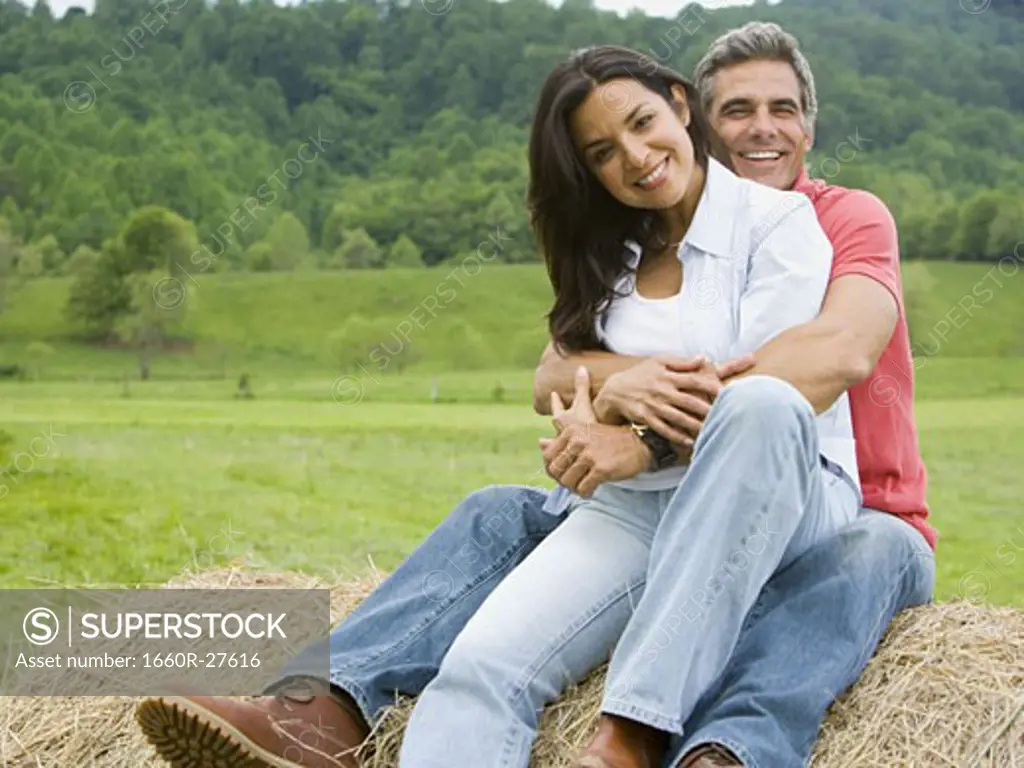 man and a woman sitting on a hay bale