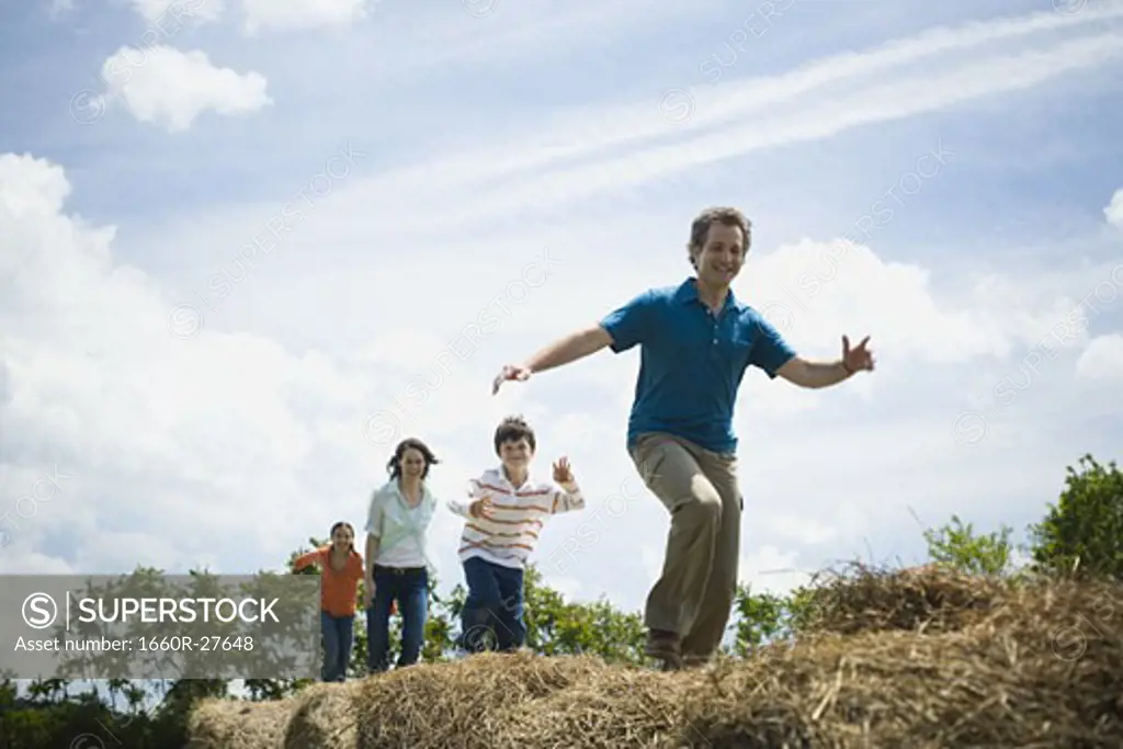 Low angle view of a man and a woman jumping with their children on hay bales