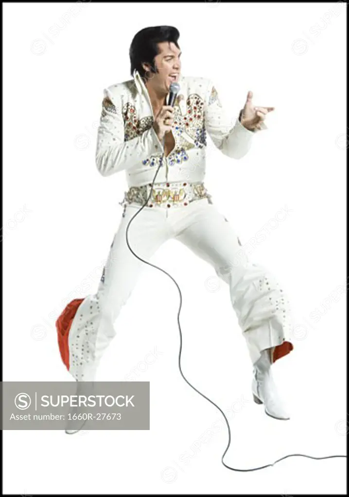 An Elvis impersonator singing into a microphone and jumping