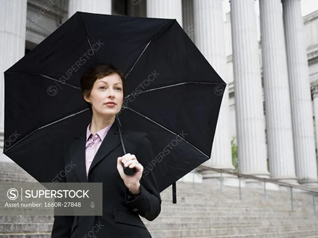 Portrait of a female lawyer standing on the steps of a courthouse and holding an umbrella