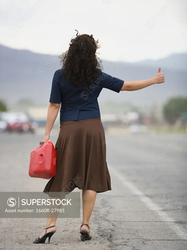 Rear view of a young woman holding a gas can and hitchhiking