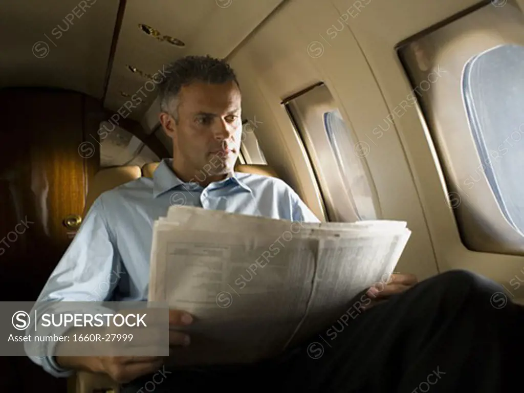 Low angle view of a businessman reading a newspaper in an airplane