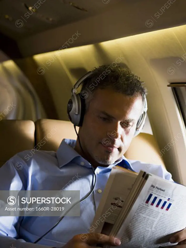A businessman listening to music on headphones and reading a magazine in an airplane