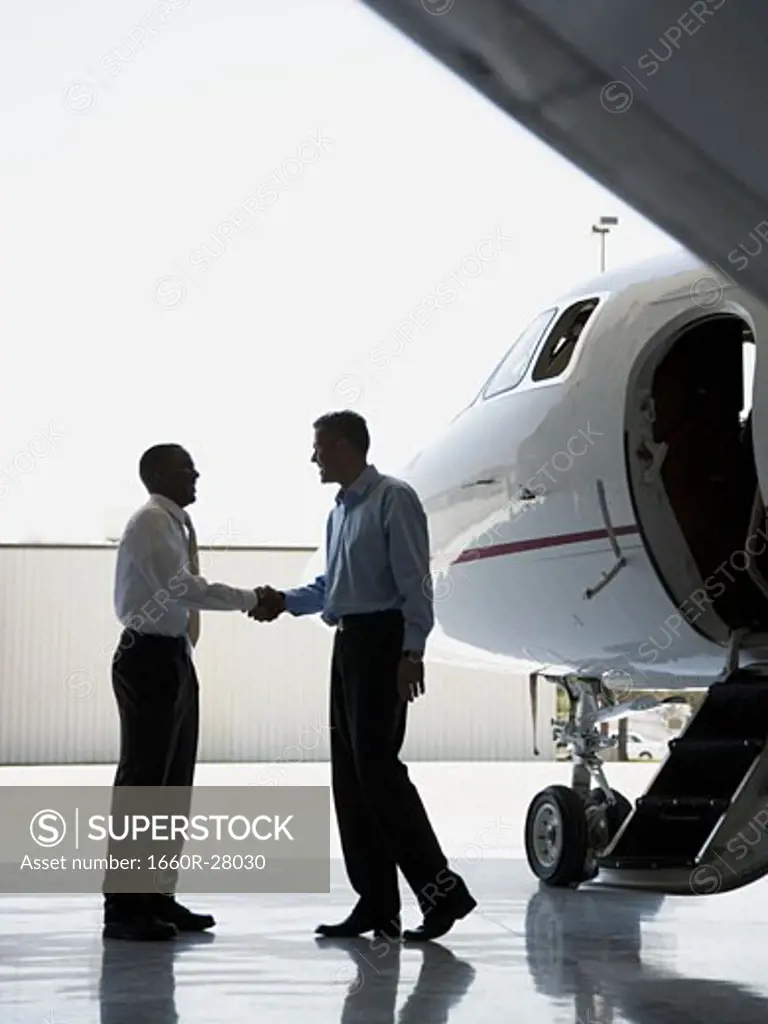 Profile of two businessmen shaking hands near an airplane