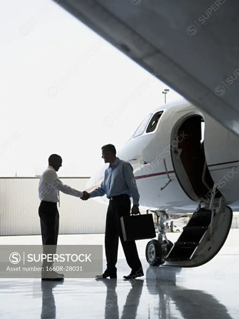 Profile of two businessmen shaking hands near an airplane