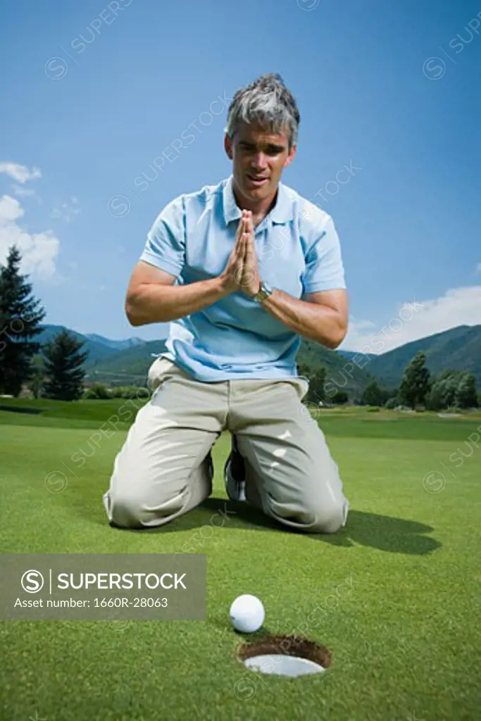 Man kneeling near a golf hole and praying