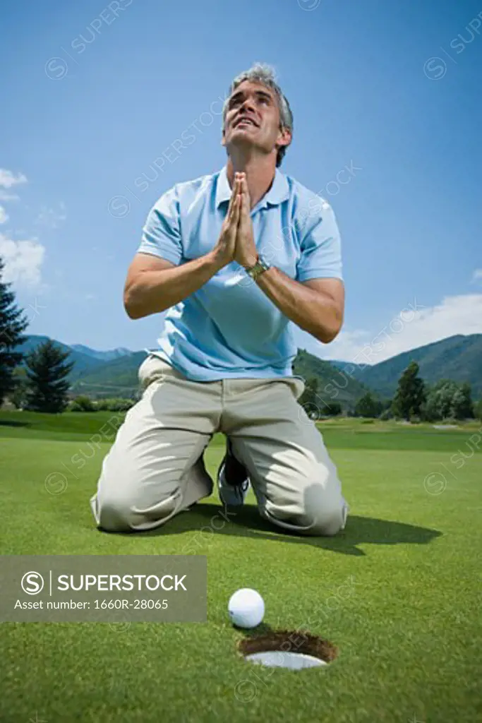 Man kneeling near a golf hole and praying