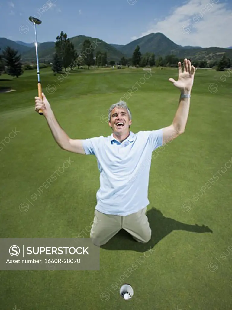 Man kneeling near a golf hole with his arms raised