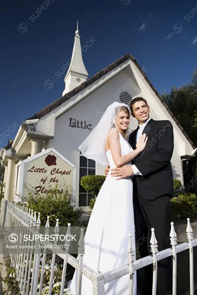 Portrait of a newlywed couple standing in front of a chapel and smiling
