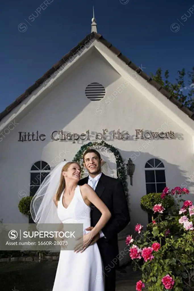 Newlywed couple standing in front of a chapel and smiling