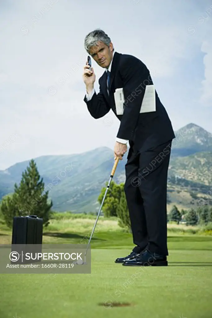 Profile of a businessman playing golf and talking on a mobile phone