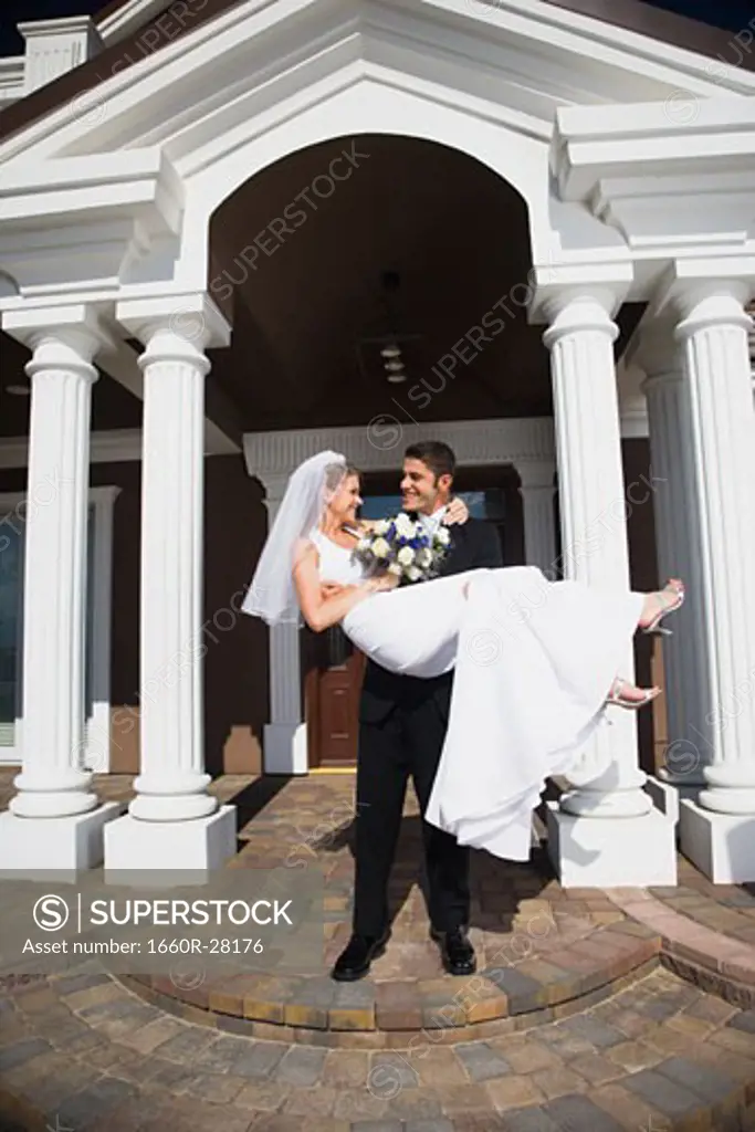 Young man carrying his bride in his arms in front of a building