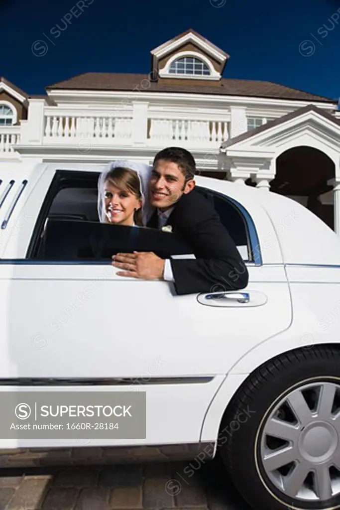 Portrait of a newlywed couple leaning out from a car window and smiling