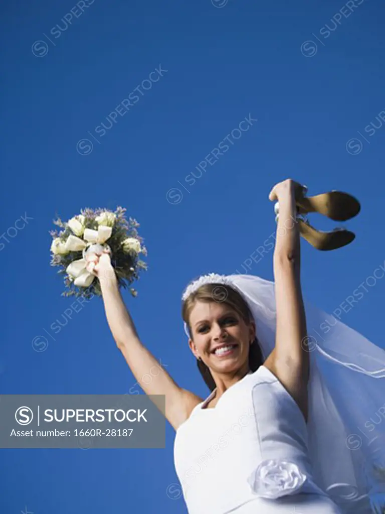 Portrait of a bride holding a bouquet of flowers and a pair of sandals